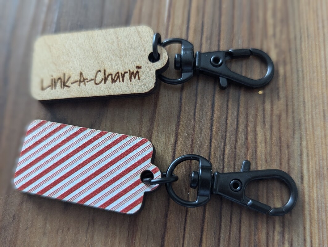An engraved wood Link-A-Charm tag and a candy-cane striped tag, both on black lobster clasps