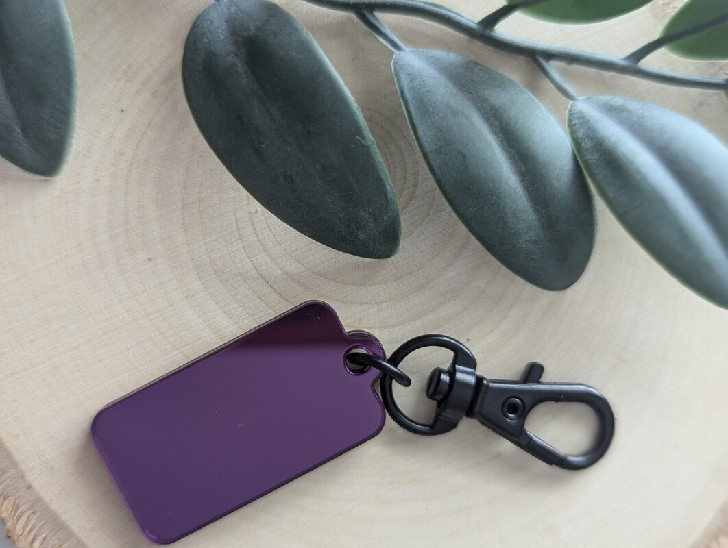 A purple acrylic Link-A-Charm tag on a wood slice beside eucalyptus leaves