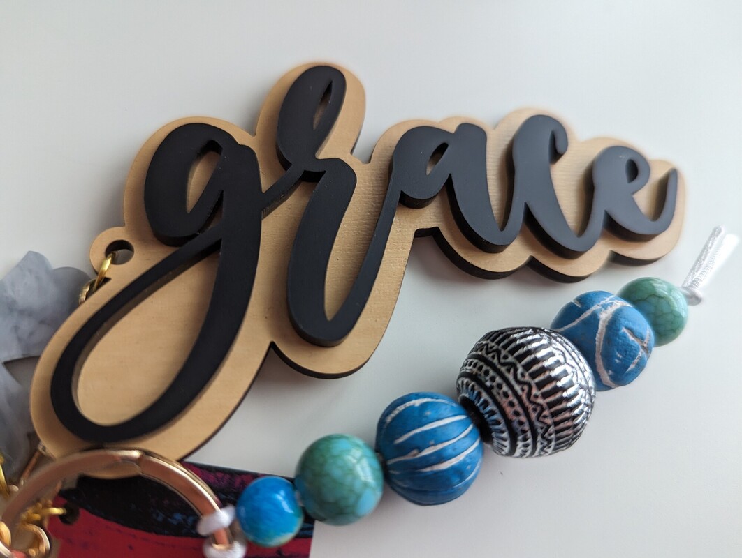 Close-up of a ‘grace’ charm in layered wood and grey acrylic with blue and turquoise beads