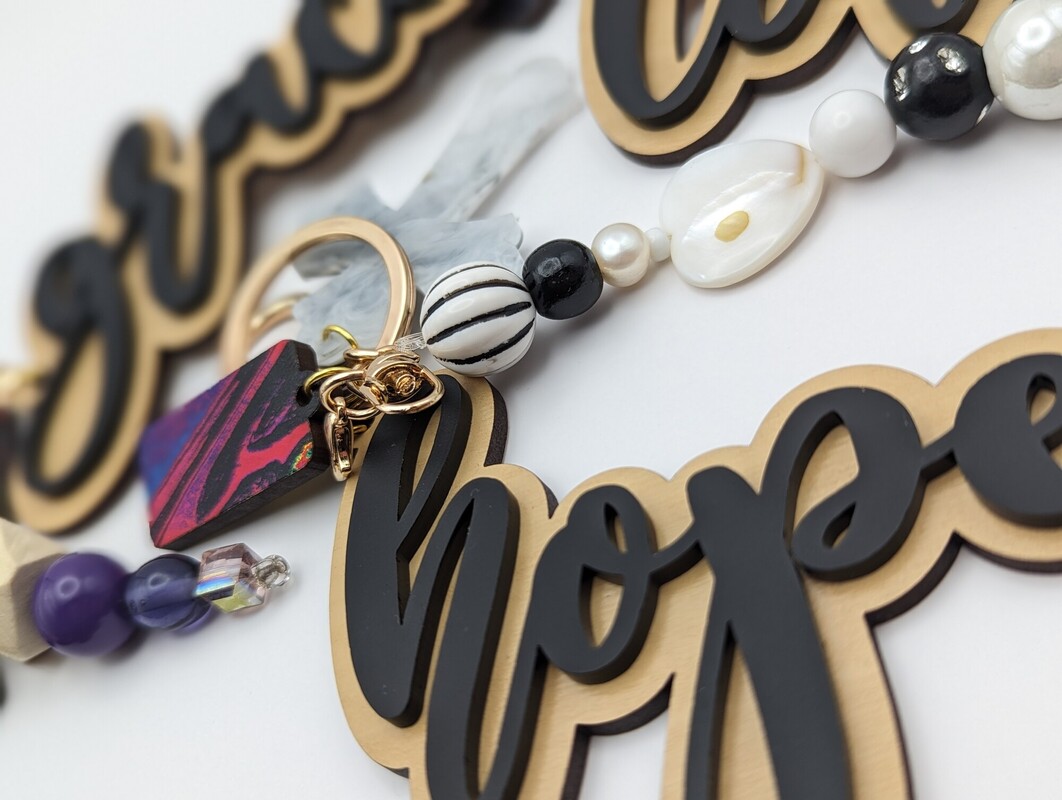 Close-up of ‘hope’ and ‘grace’ charms with pearl and black striped beads
