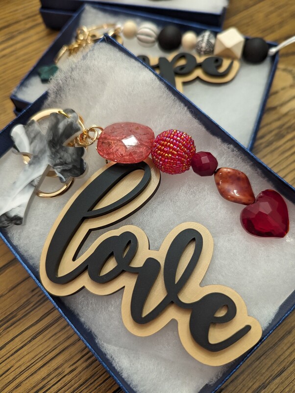 A ‘love’ charm with red and coral beads resting in a navy gift box