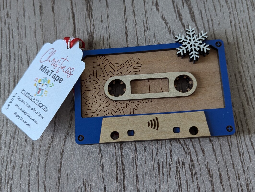 A wood and blue acrylic cassette-tape NFC ornament with a snowflake and a Christmas Mixtape hang tag